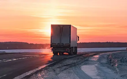 Refrigerated truck driving on a winter road at sunrise, representing cold chain logistics and temperature-controlled transport.