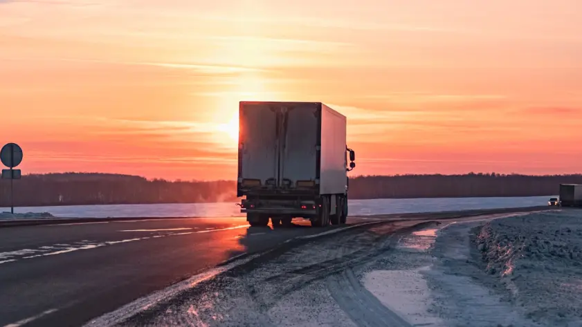 Refrigerated truck driving on a winter road at sunrise, representing cold chain logistics and temperature-controlled transport.