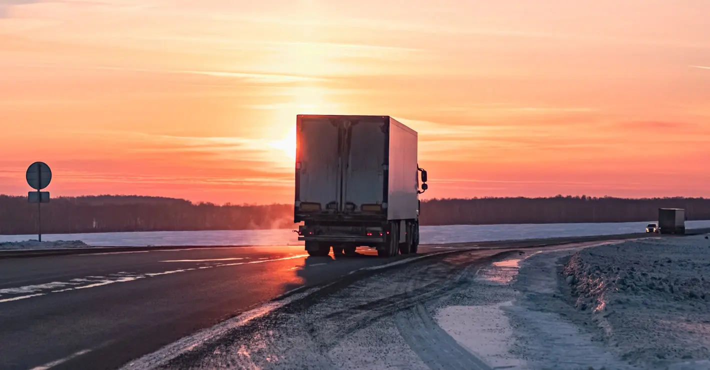 Refrigerated truck driving on a winter road at sunrise, representing cold chain logistics and temperature-controlled transport.